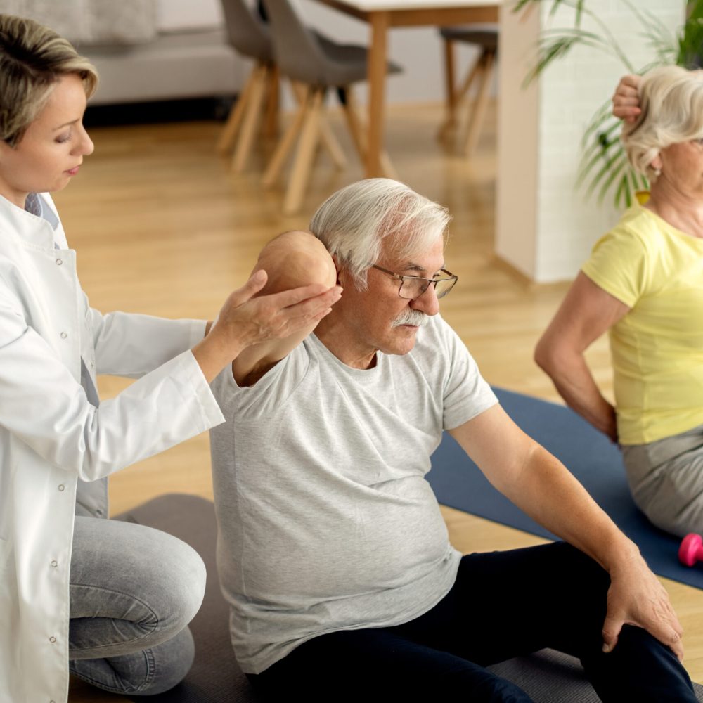 Female physiotherapist helping to senior couple with exercising at home.